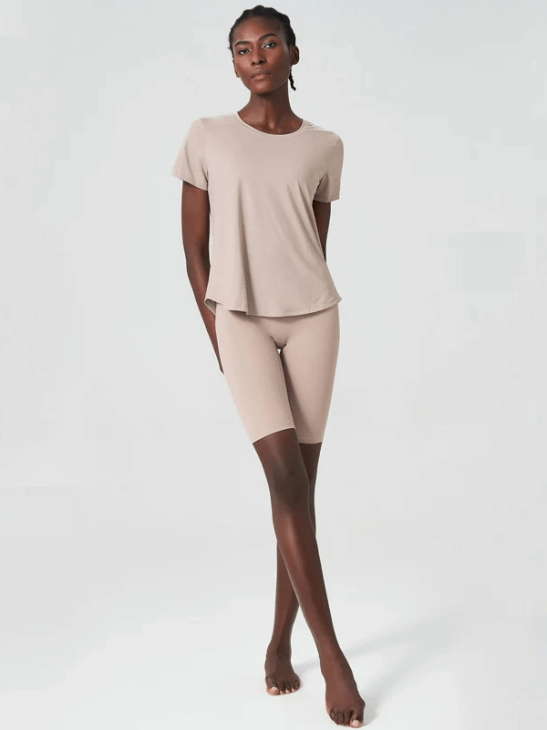 Woman wearing a beige two-piece yoga set made of breathable Lycra, featuring short sleeves and quick-dry properties for gym or yoga sessions.